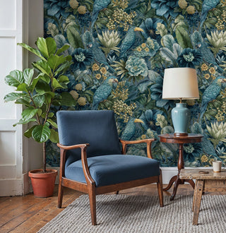 Tropical parrot wallpaper with lush teal botanicals and gold berries in a cozy room with blue armchair and fiddle leaf fig