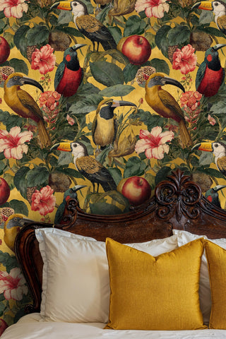 Tropical toucan wallpaper with hibiscus and fruit on gold, in a bedroom with carved wood headboard