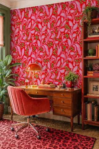 Vibrant acanthus pattern wallpaper in red and pink shown in a home office with wooden desk