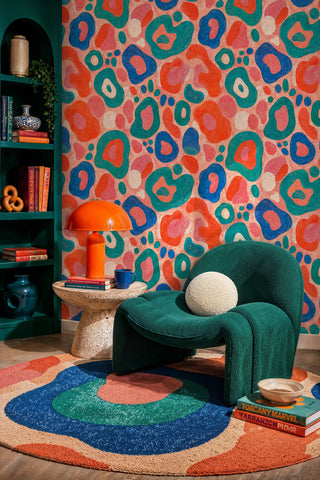 Vibrant organic shapes wallpaper in coral and blue displayed in a reading nook with teal bookshelf and orange lamp