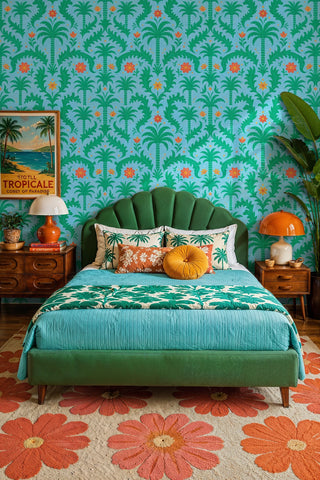 Vibrant palm tree damask wallpaper in blue and green with orange blooms, styled in a bedroom with scalloped headboard