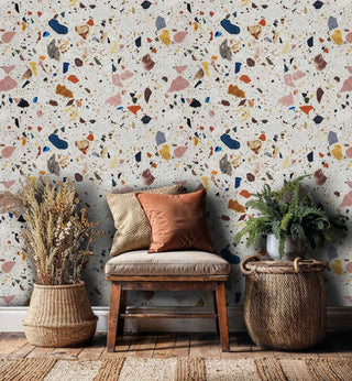 Vibrant terrazzo pattern wallpaper with scattered stone chips, shown in living room with natural woven baskets