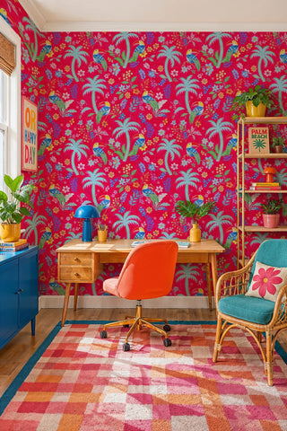 Vibrant tropical bird wallpaper with lush florals on hot pink, in a home office with wooden desk and rattan chair