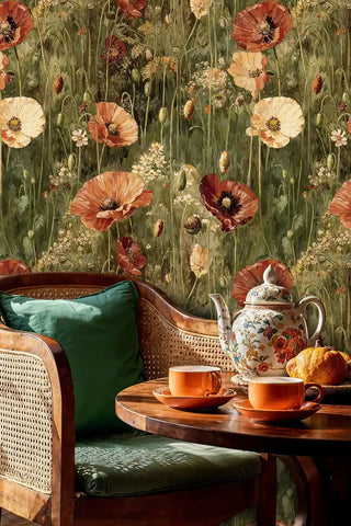 Vintage poppy meadow wallpaper with coral and cream blooms on sage green, shown in cozy seating area with woven chair