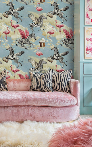 whimsical flying zebras and flamingos wallpaper in blue and pink, shown in living room with pink sofa