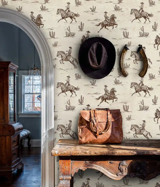 Wild west wallpaper with cowboys and cacti pattern displayed in entryway with leather bag and horseshoes