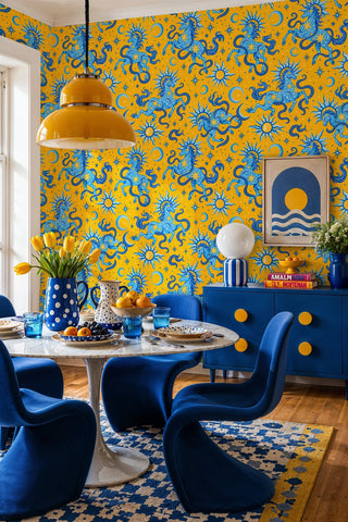 Yellow celestial horse wallpaper with blue sun motifs, in a dining room with marble tulip table and blue chairs